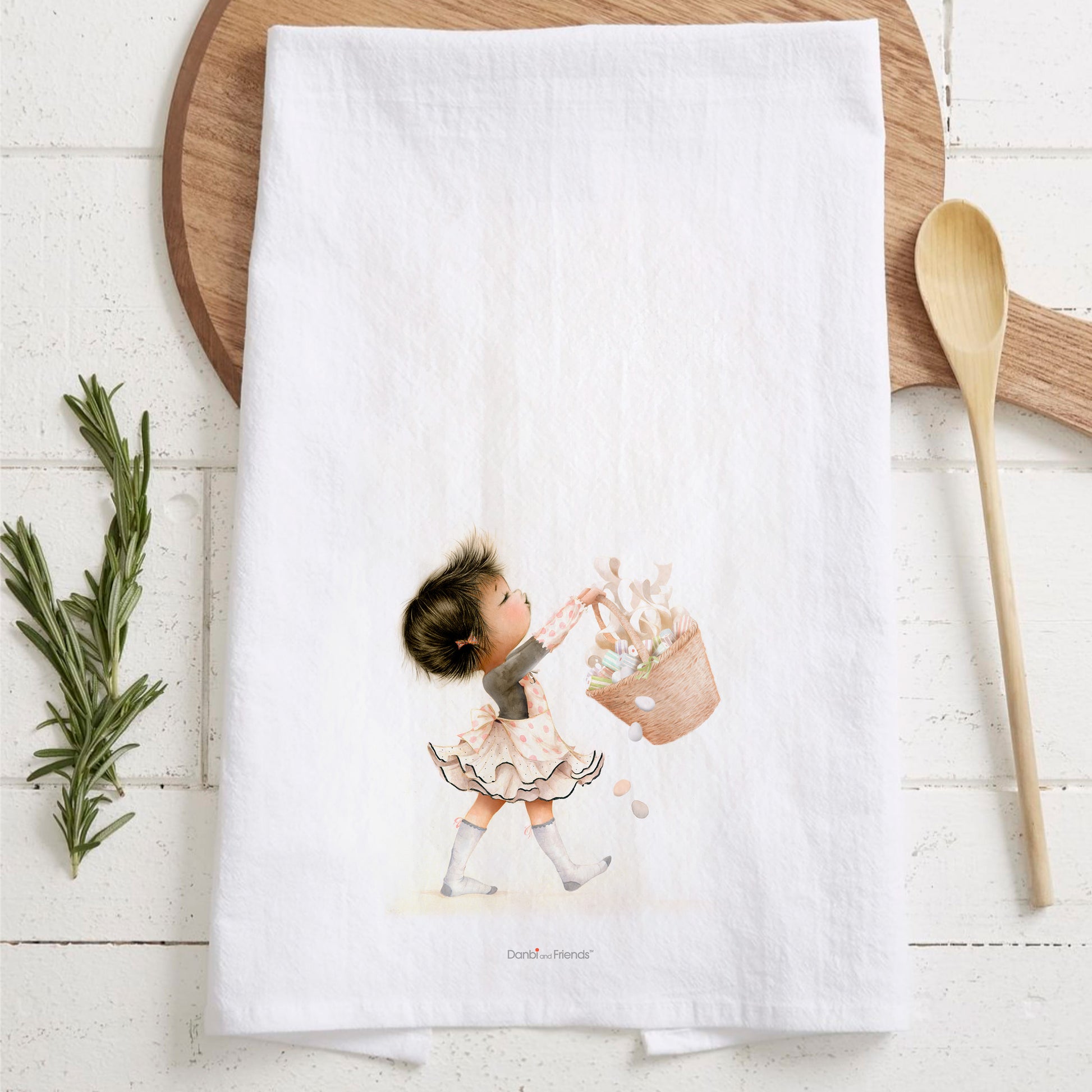 White towel with a child illustration on a wooden surface with a wooden spoon and rosemary.