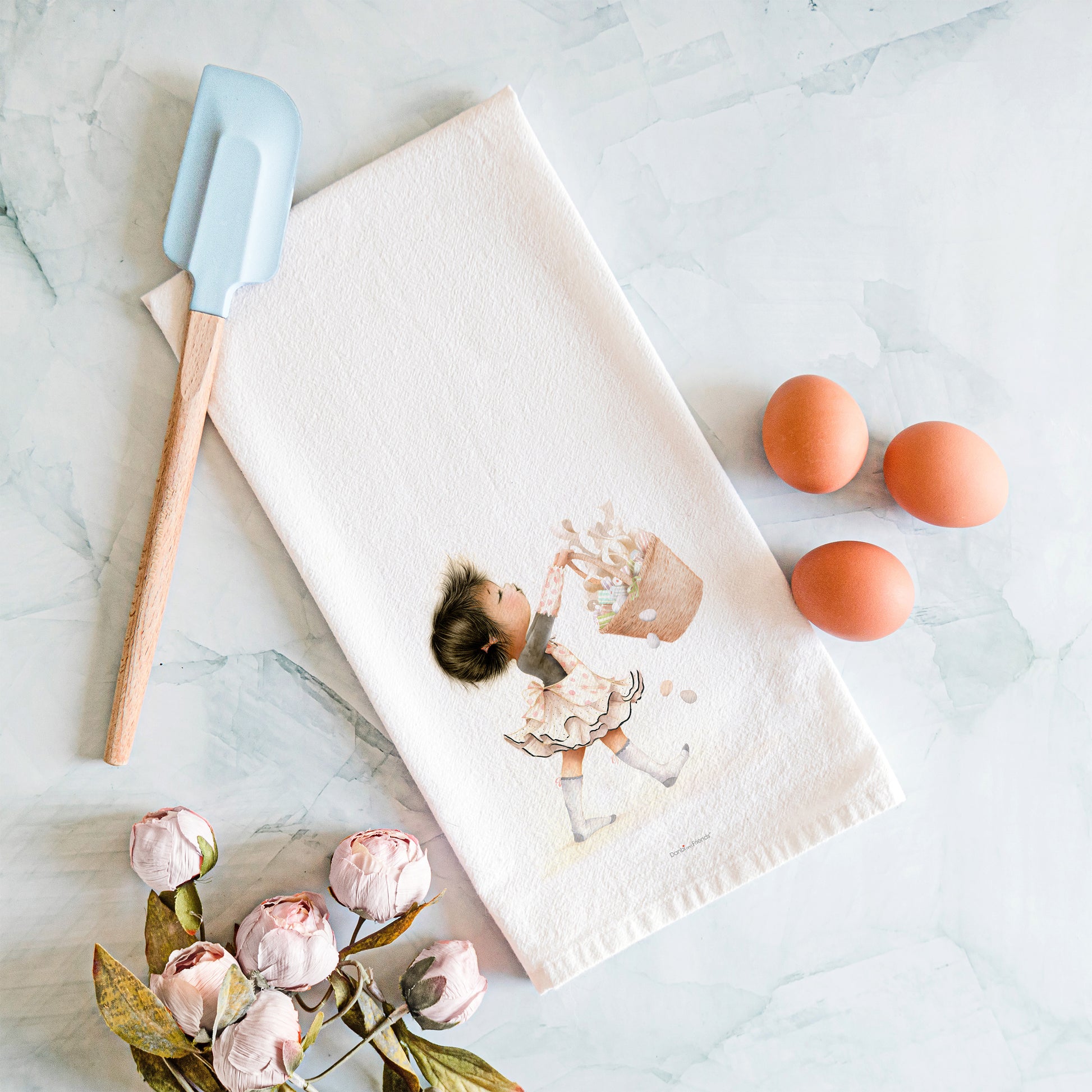 Kitchen towel with a child and cake illustration, spatula, and eggs on a marble surface