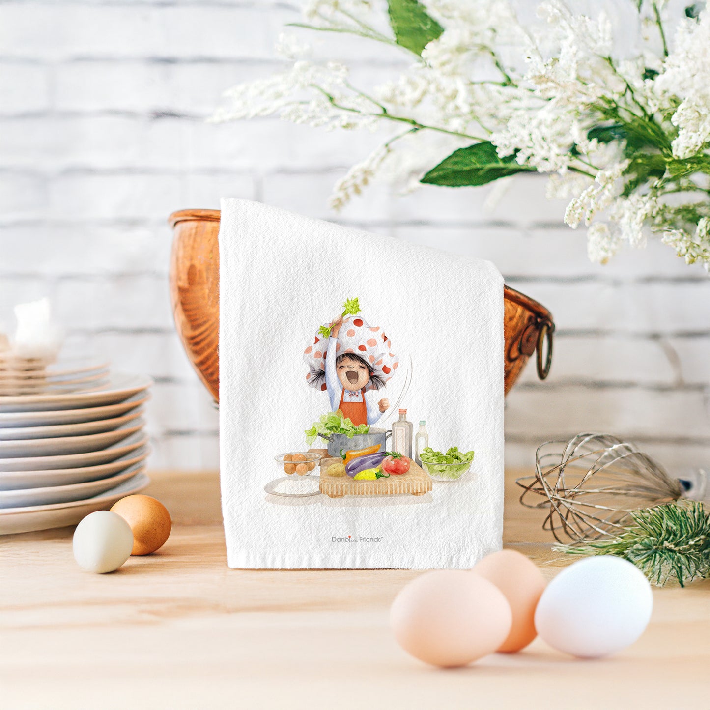Kitchen towel with a cartoon character holding a basket of vegetables on a kitchen counter with eggs and a whisk.