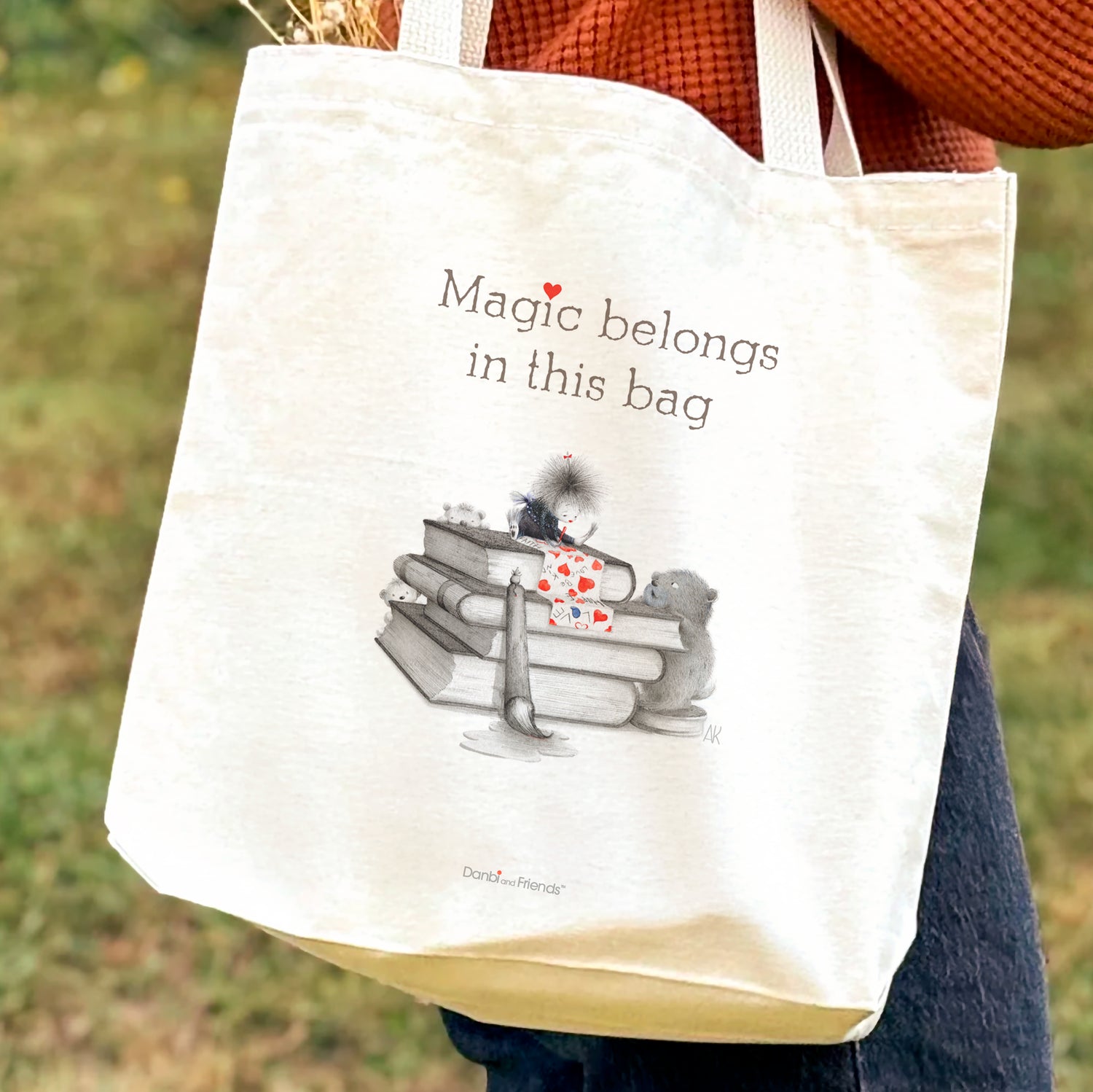 Tote bag with 'Magic belongs in this bag' text and book illustration held by a person outdoors.