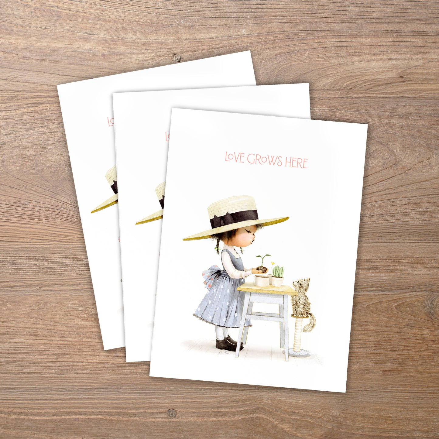 Three greeting cards with illustrations of a girl and a cat on a wooden surface