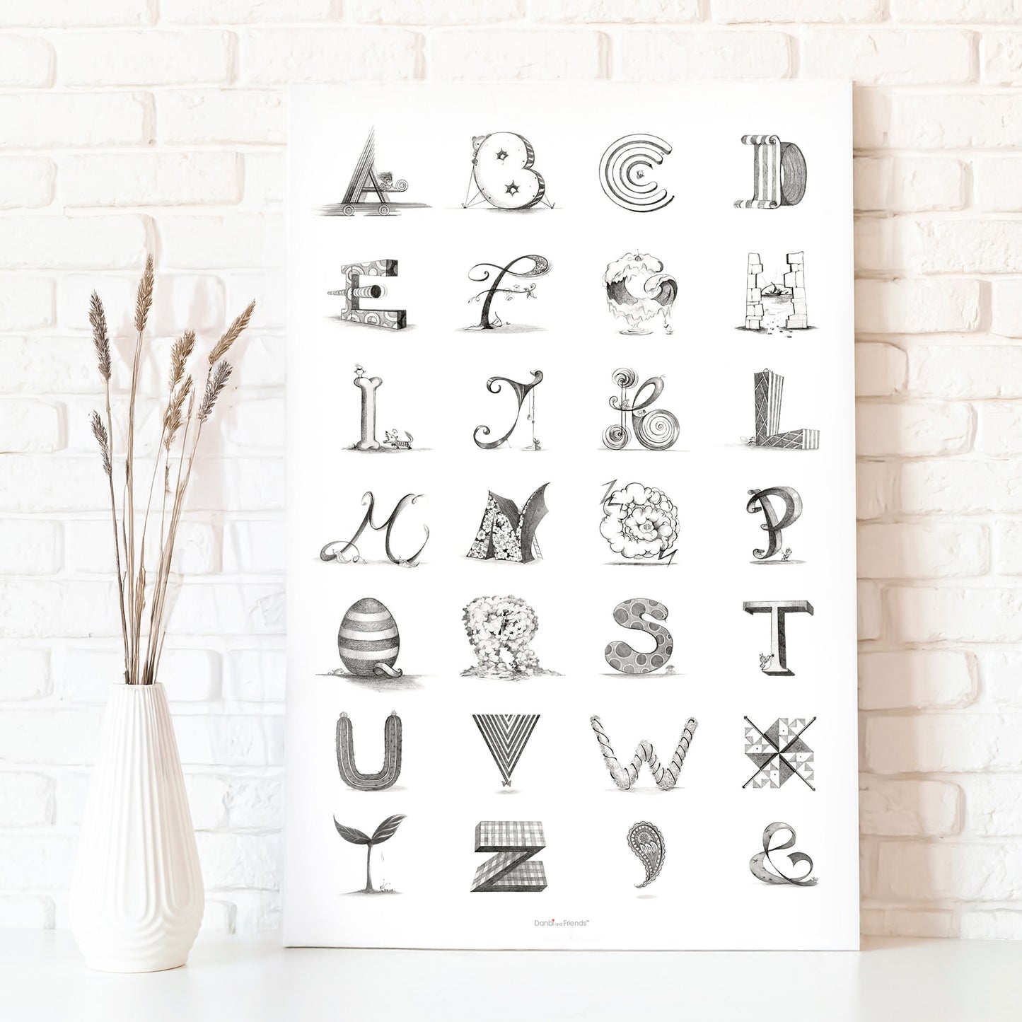 Black and white alphabet poster on a white brick wall with a vase of dried plants.