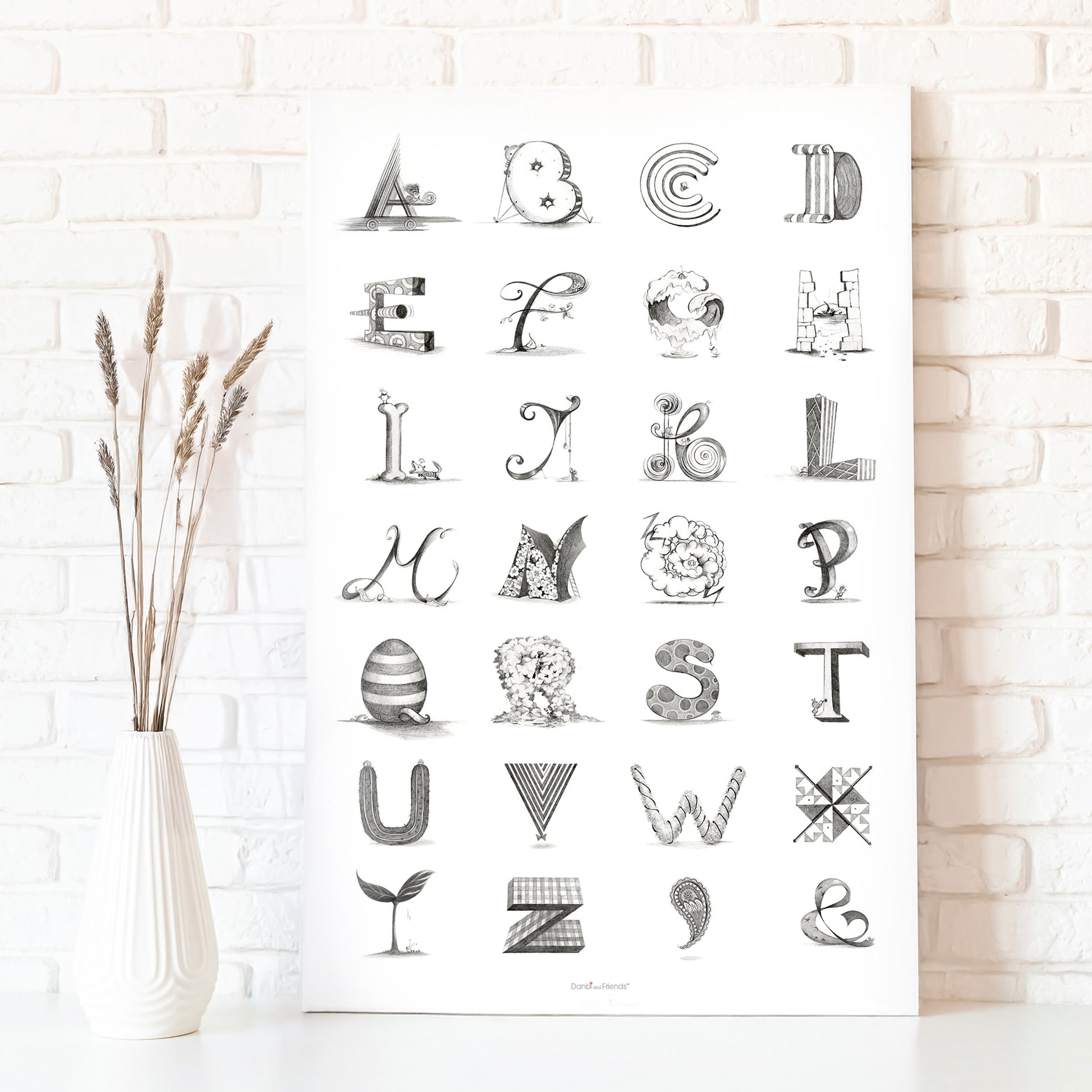 Black and white alphabet poster on a white brick wall with a vase of dried plants.