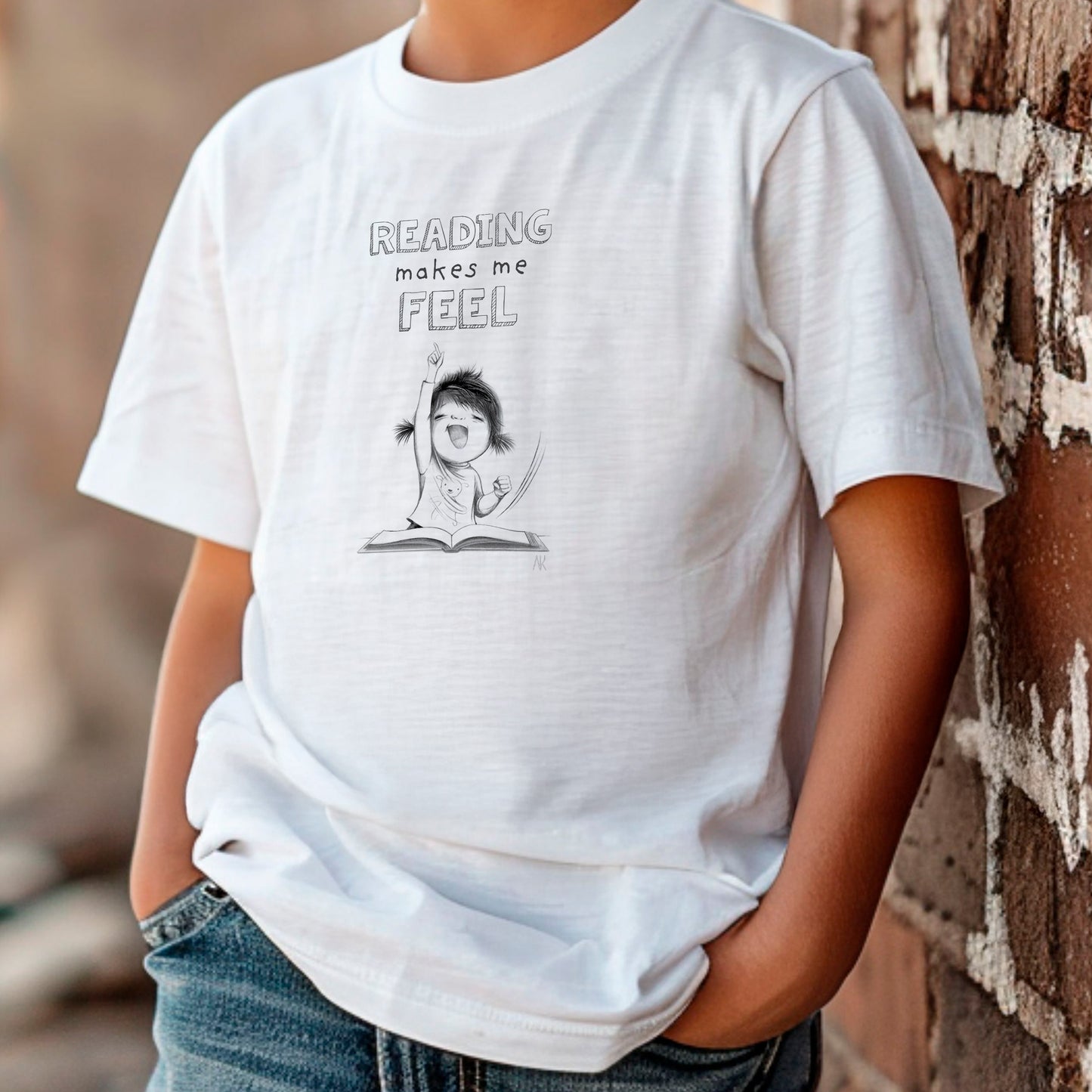 Kid is wearing a white t-shirt with a graphic and text 'READING makes me FEEL' against a natural background.