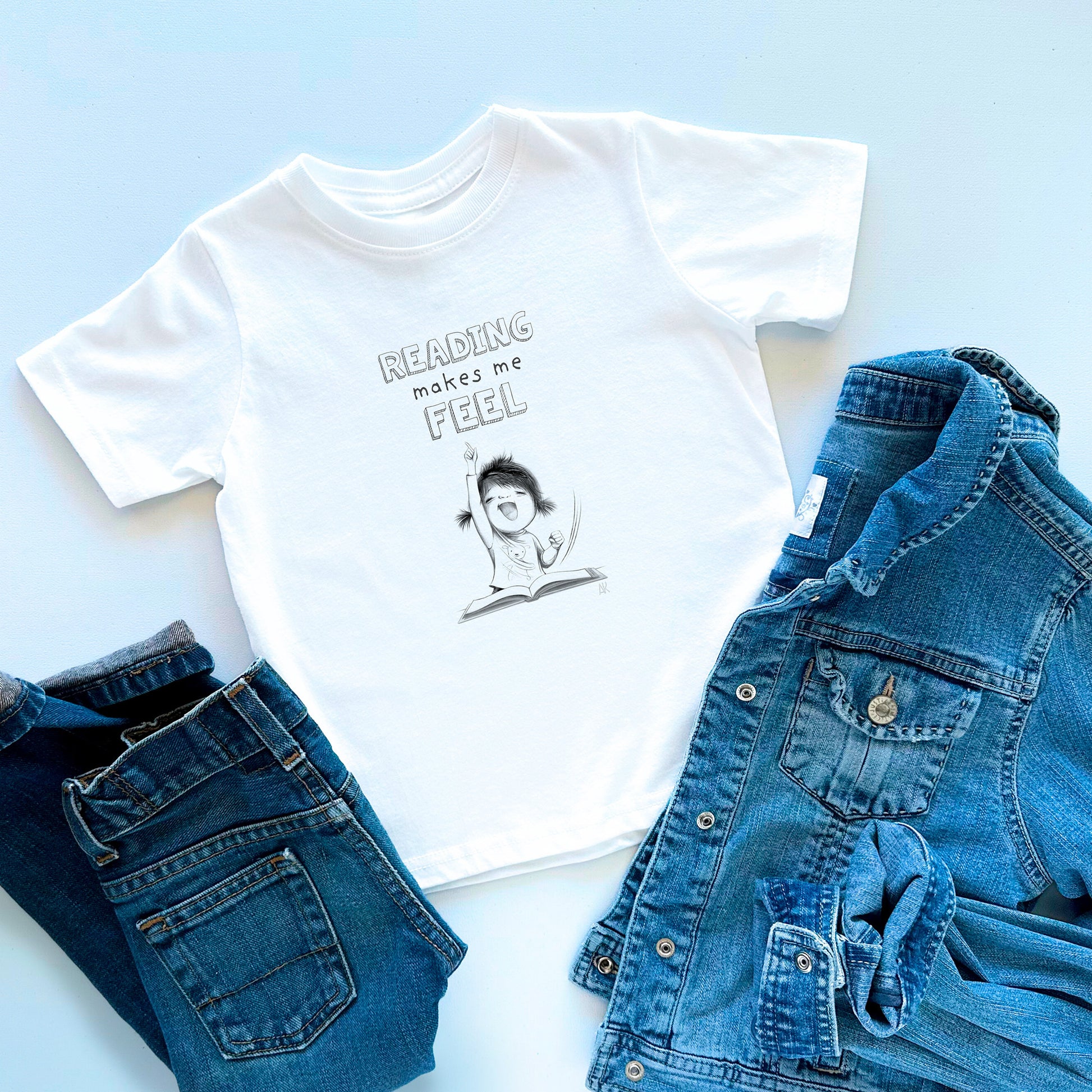 White t-shirt with 'Reading makes me feel' graphic and text, paired with blue jeans and denim jacket on a light blue background.