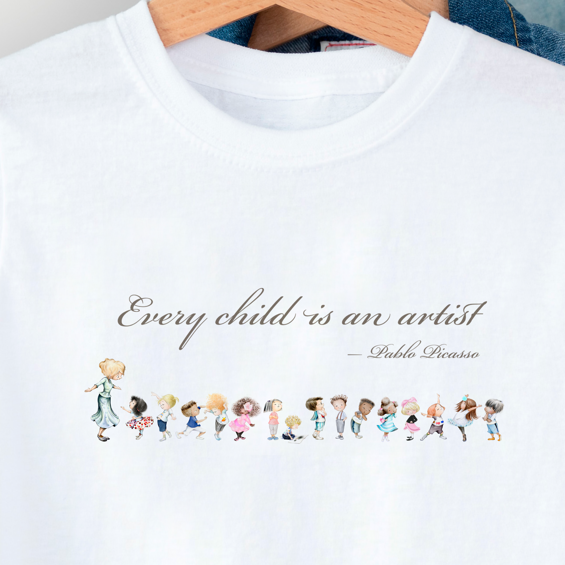 White t-shirt with illustrations of children and a quote by Pablo Picasso on a hanger.